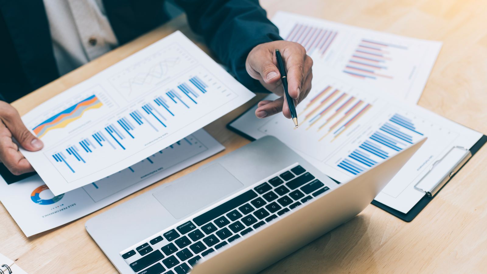 Financial statements and charts on a desk beside a laptop