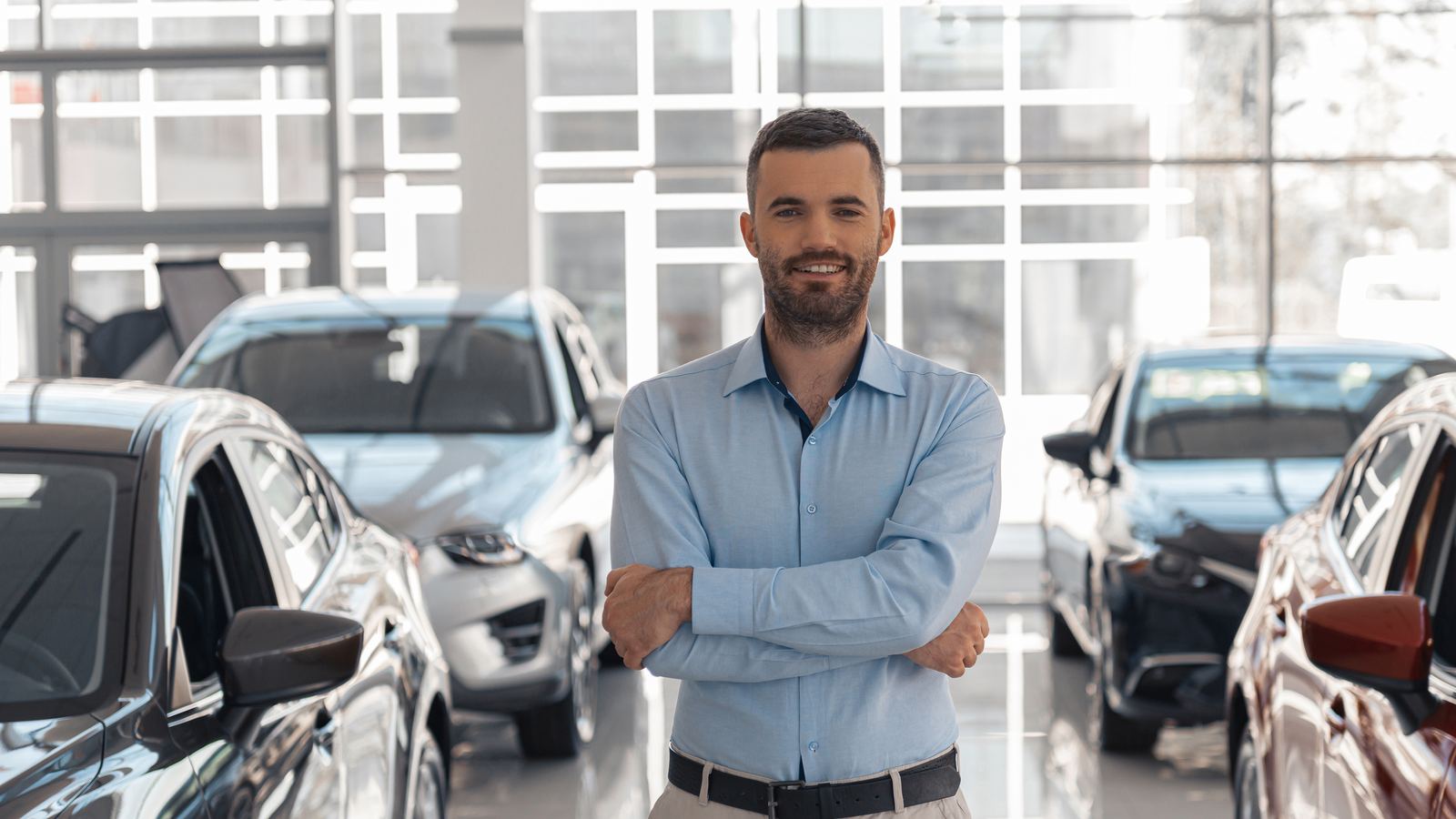 A general manager standing among vehicles in a dealership showroom