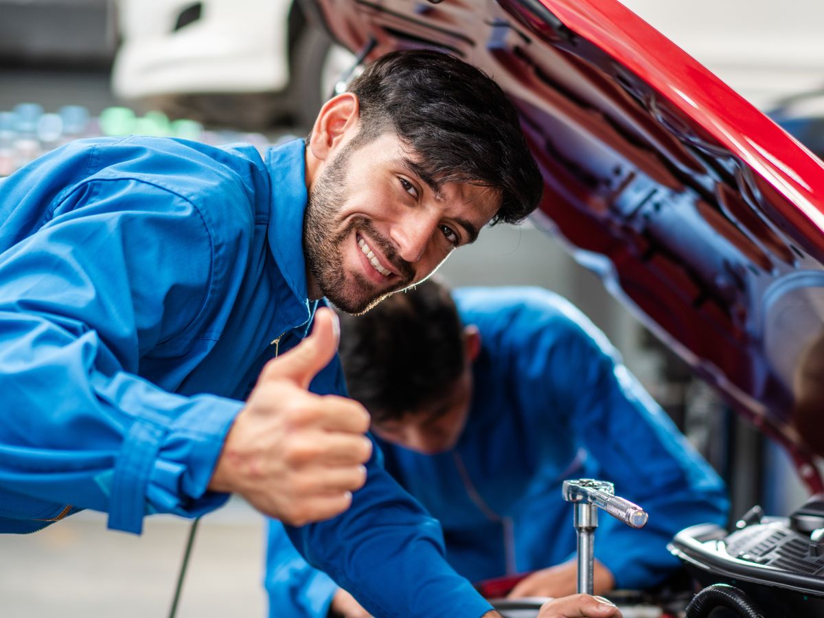A technician giving a thumbs up under an open hood