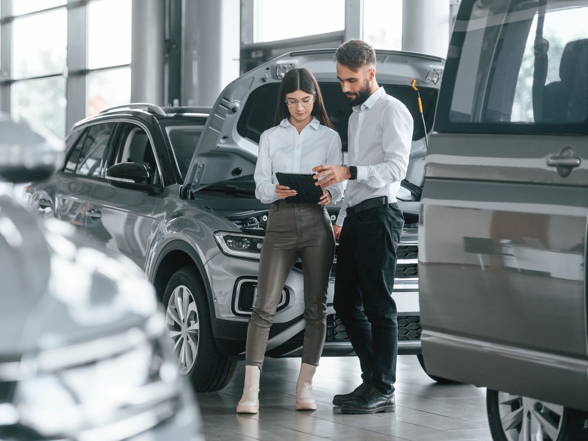 A dealership employee reviewing a tablet with a customer beside an SUV