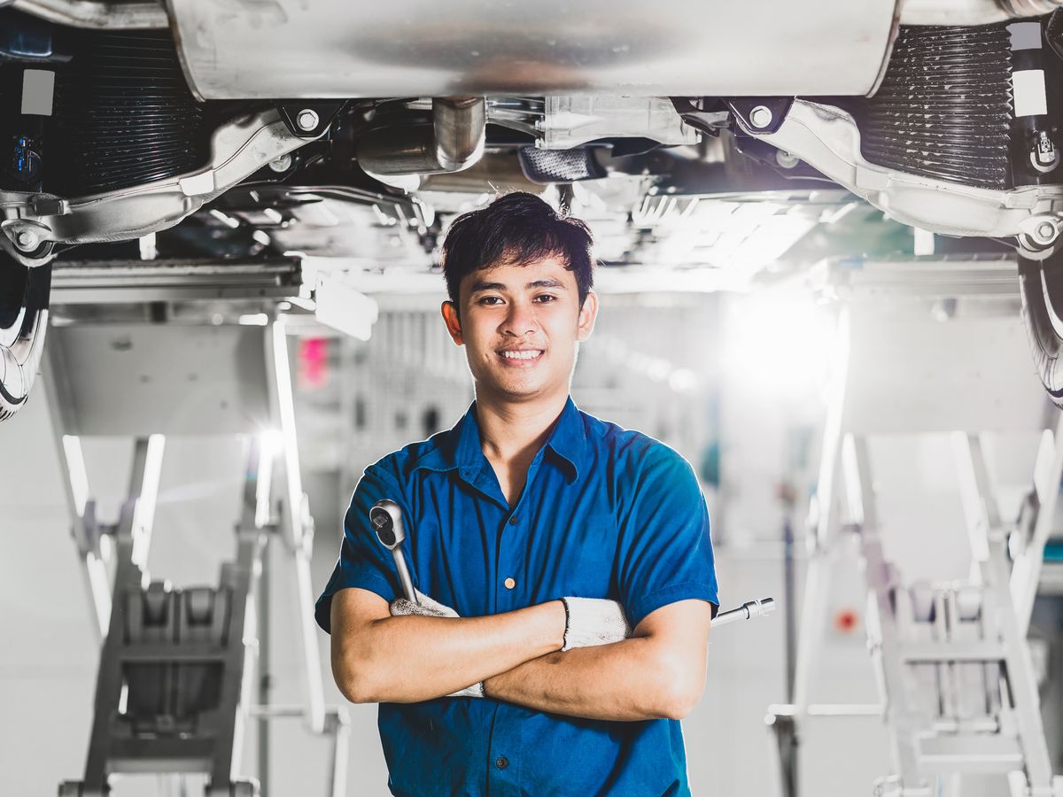 A smiling technician standing under a vehicle lift