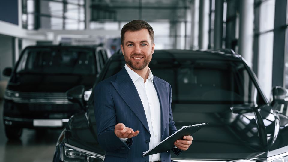 A general manager standing beside new vehicles in the showroom