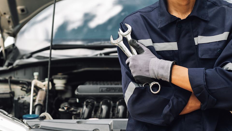 A technician holding wrenches beside an open engine bay