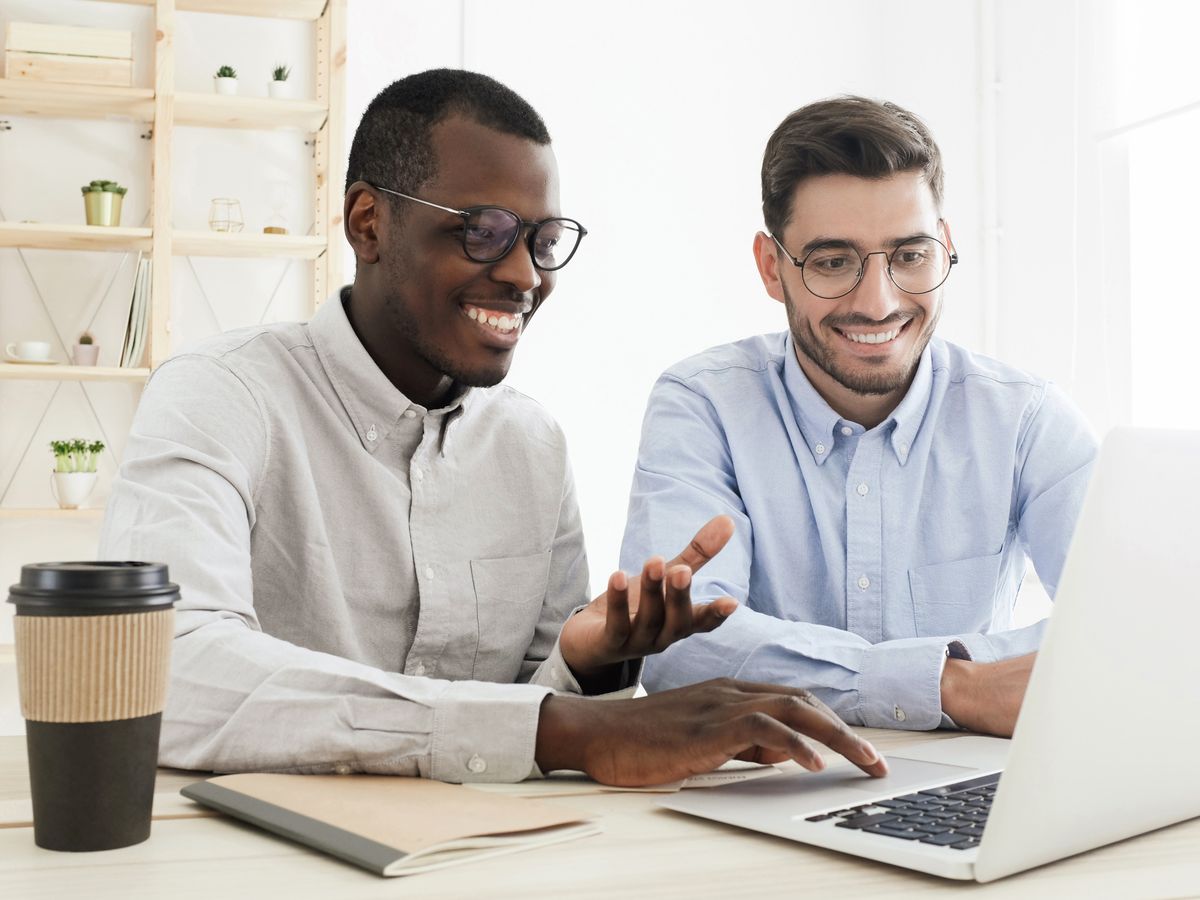 A mentor walking a newer employee through work on a laptop